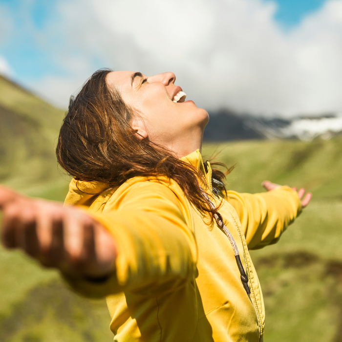 Woman with PCOS lifts arms in the air and smiles on a hike