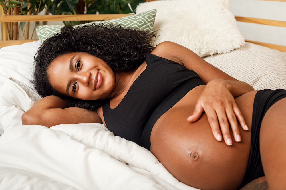 Pregnant woman lies on her side, smiling holding her belly