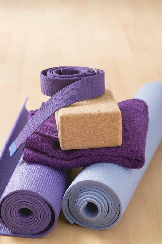 Two purple yoga mats with a towel, cork block and yoga strap resting on top.